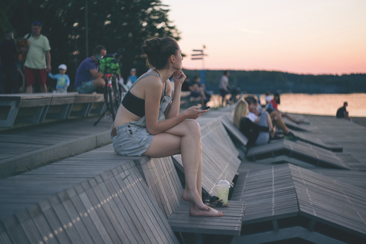 γυναίκα κάθεται σε παγκάκι και βλέπει το ηλιοβασίλεμα