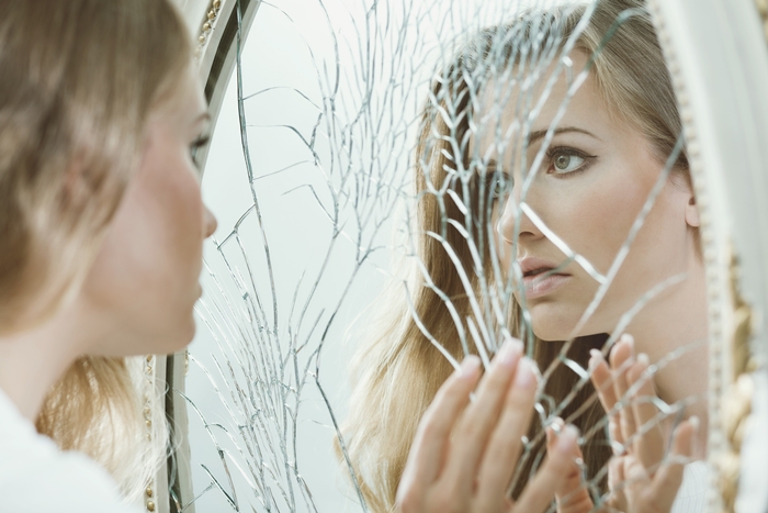 γυναίκα κοιτάζει ένα ραγισμένο καθρέπτη και πάσχει από οριακή διαταραχή προσωπικότητας
