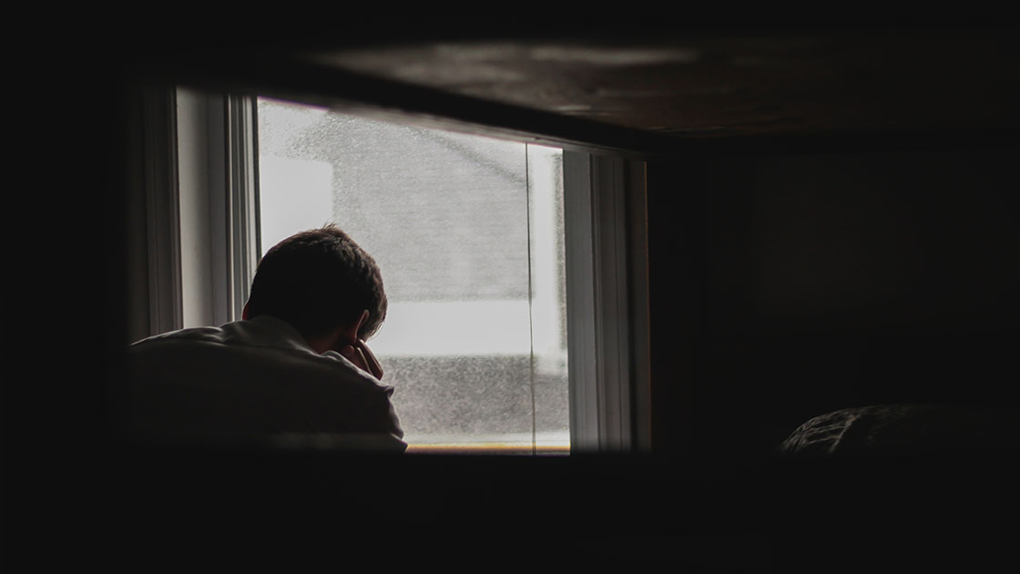 άντρας κοιτάζει έξω από το παράθυρο και το σώμα του μιλάει την γλώσσα της κατάθλιψης