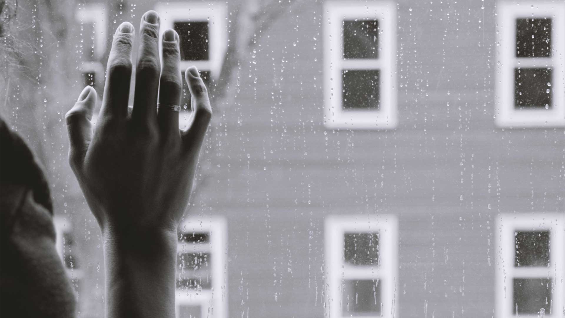 ασπρόμαυρη φωτογραφία που απεικονίζει ένα χέρι να ακουμπάει στο παράθυρο ενώ βρέχει