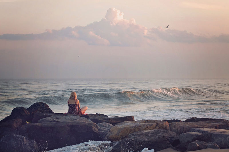 γυναίκα που κάθεται σε ένα βράχο δίπλα στη θάλασσα το απόγευμα Και έχει πάρει διάλειμμα από την ψυχοθεραπεία της