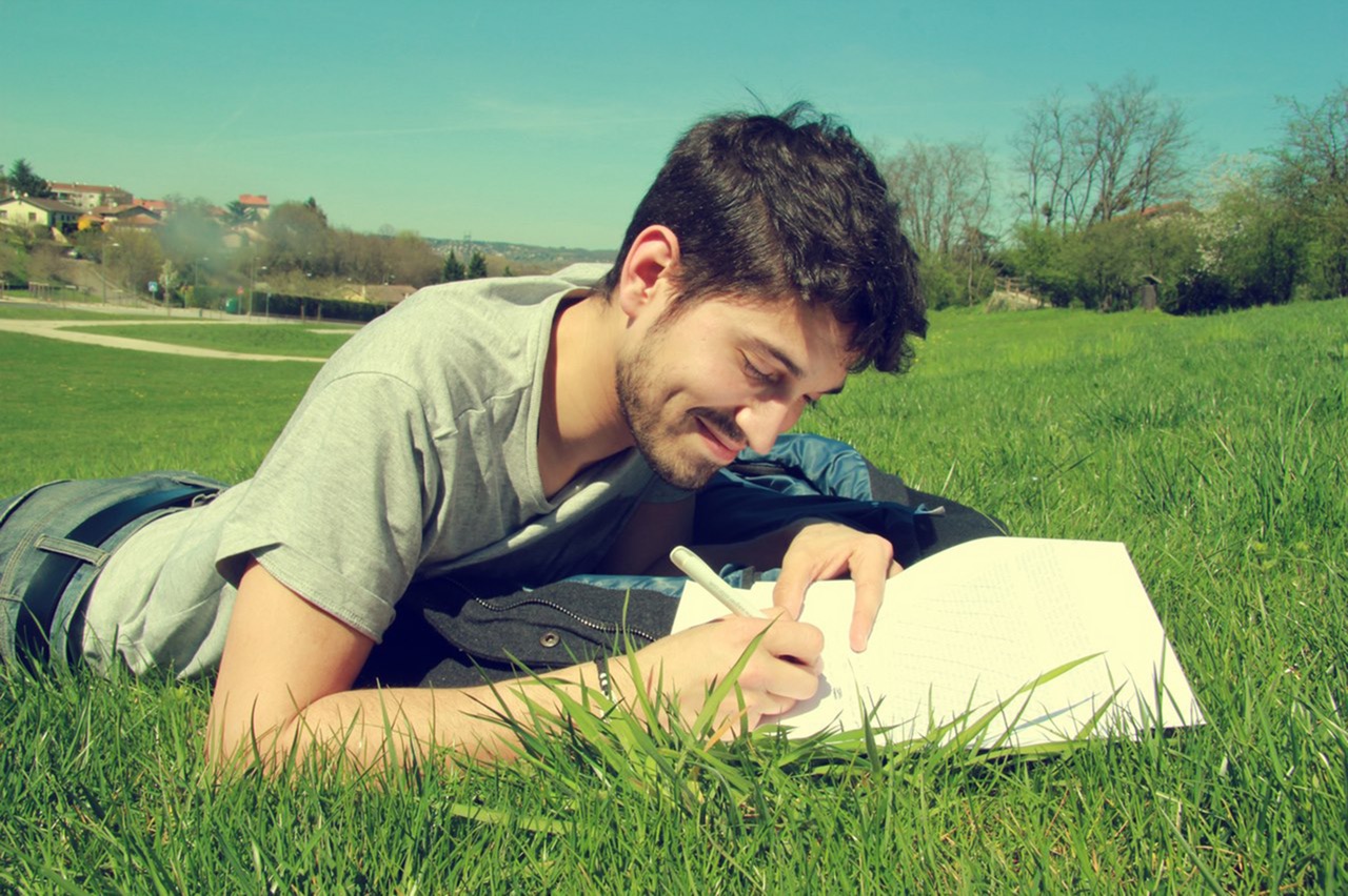φωτογραφία νεαρού που είναι ξαπλωμένος στο γρασίδι και γράφει, αξιοποιώντας στο έπακρο την ψυχοθεραπεία 