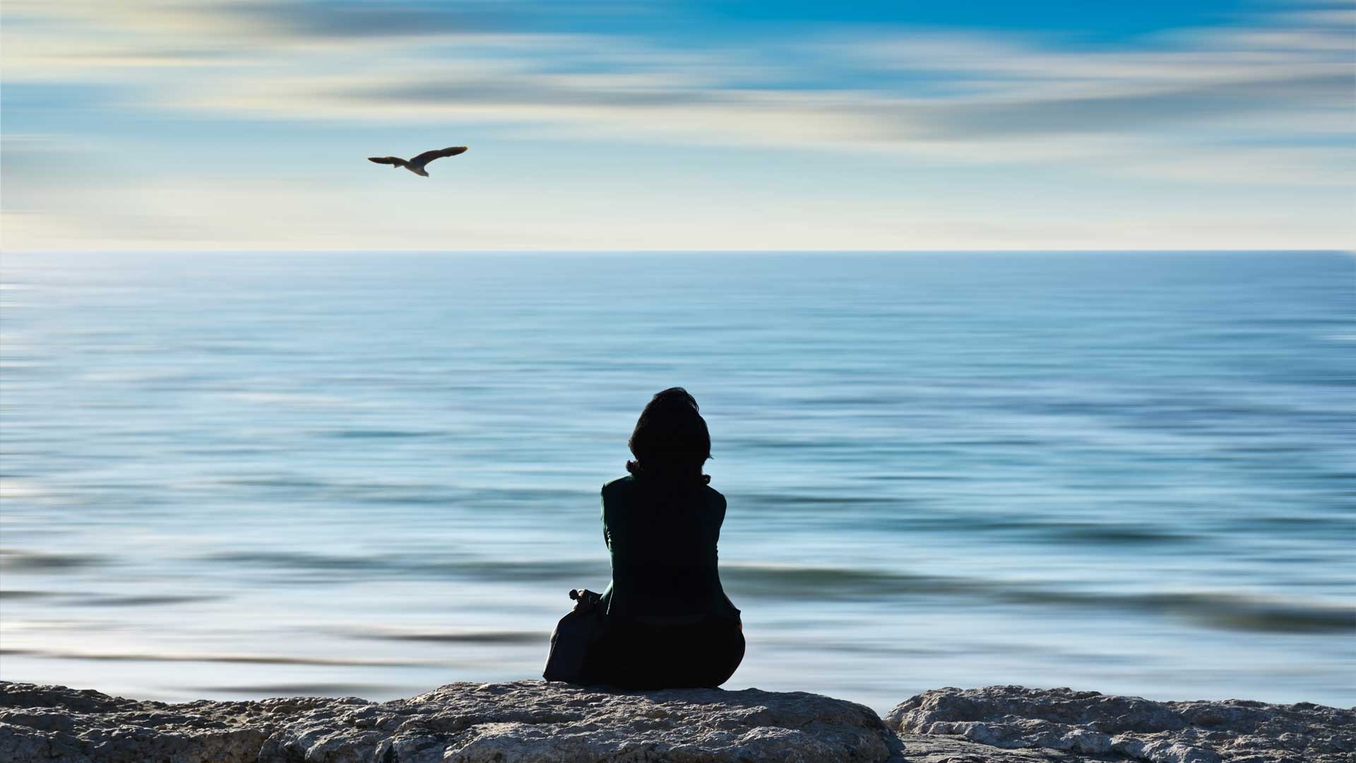 γυναίκα που κάθεται στα βράχια και ατενίζει τη θάλασσα