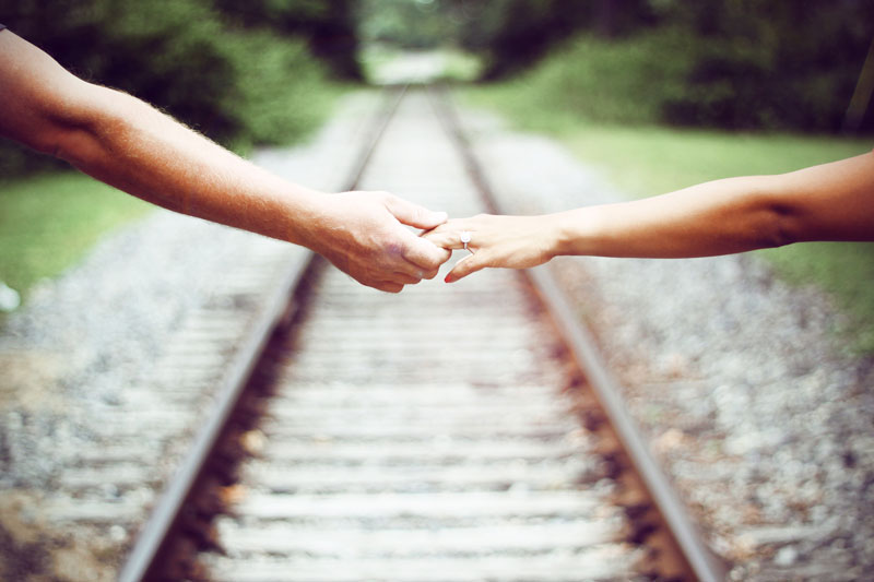 άνδρας και γυναίκα που κρατιούνται πάνω από σιδηροδρομικές γραμμές και δείχνουν την συναισθηματική ασφάλεια στην σχέση τους