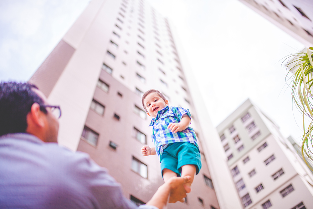 πατέρας κρατάει στο ένα χέρι το παιδί του και το σηκώνει ψηλά με φόντο έναν ουρανοξύστη