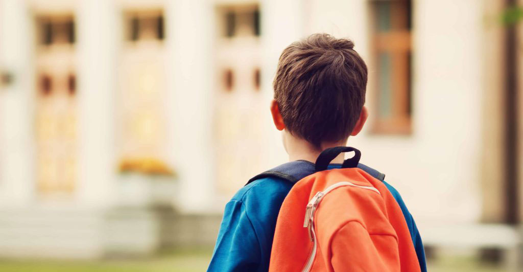 παιδί με πορτοκαλί τσάντα στον ώμο κοιτάζει το σχολείο του