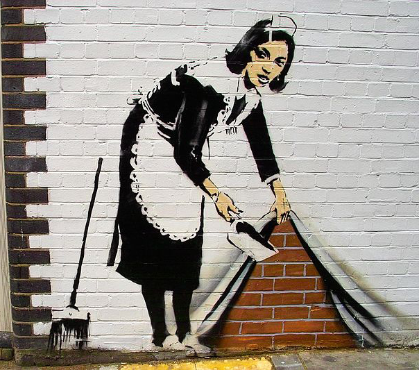 γκράφιτι γυναίκας ντυμένης καμαριέρας σε τοίχο που κρύβει κάτω από το σεντόνι τα σκουπίδια
