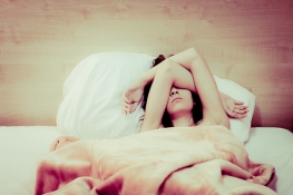 γυναίκα ξαπλωμένη στο κρεββάτι καλύπτει το πρόσωπό της με τα χέρια της