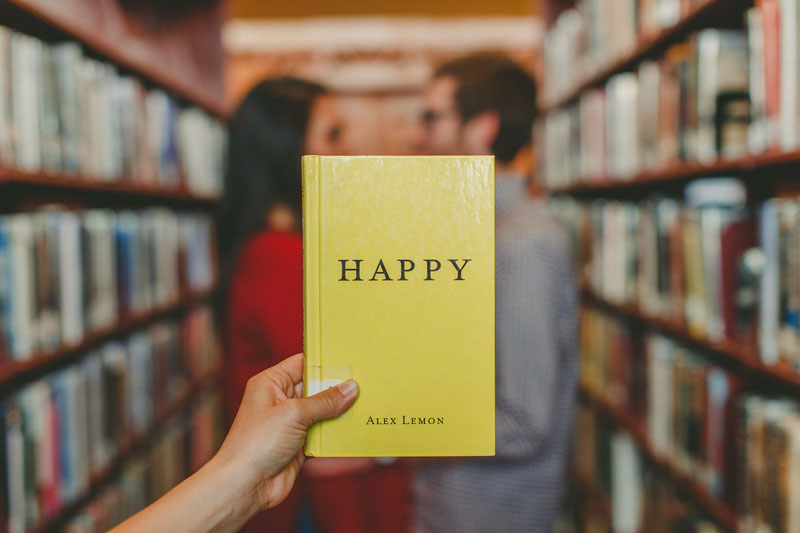 βιβλίο με τίτλο happy μπροστά από ζευγάρι σε βιβλιοθήκη