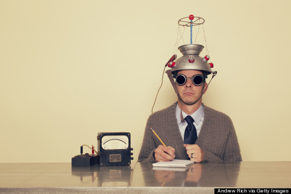 άνδρας που κάθεται σε γραφείο με ειδικό σιδερένιο καπέλο εργαστηρίου που συνδέεται με καλώδια και φοράει γυαλιά