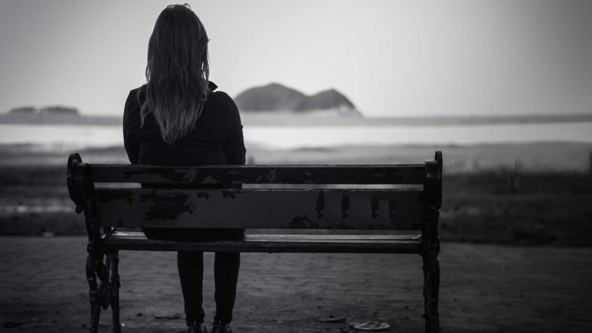 γυναίκα κάθεται σε ένα παγκάκι με θέα τη θάλασσα