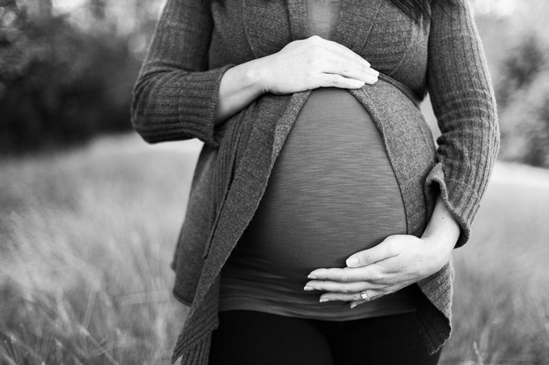 έγκυος γυναίκα κρατάει την κοιλιά της σε ασπρόμαυρο φόντο